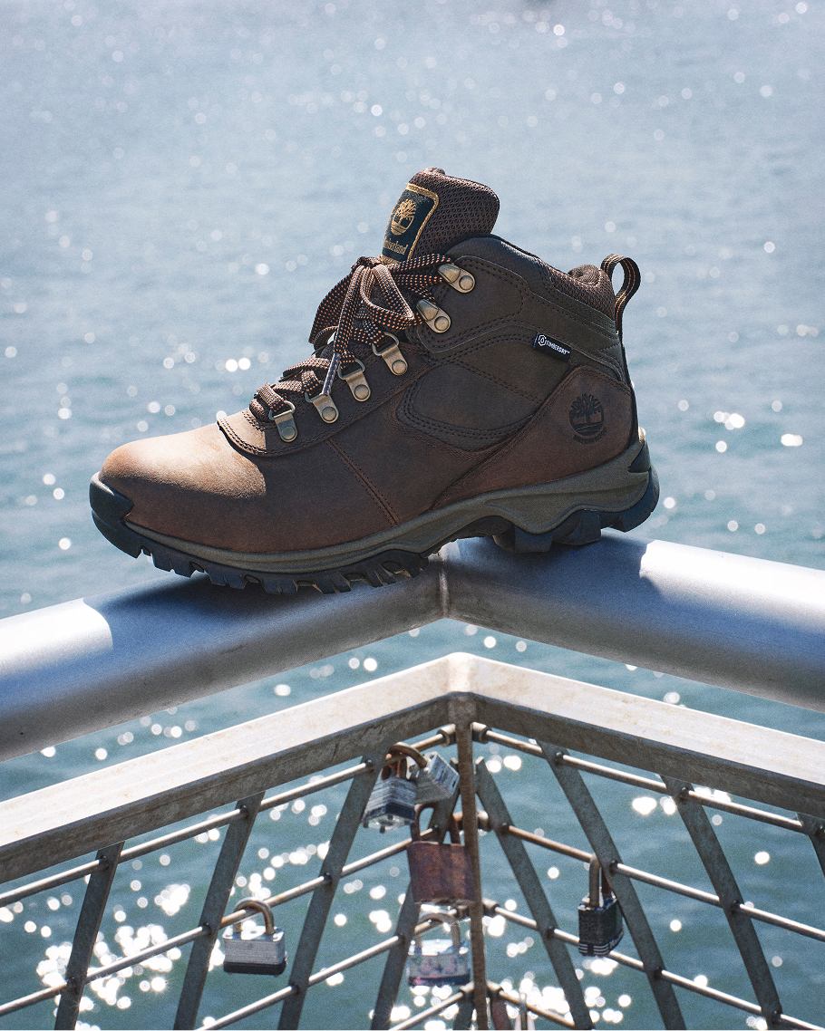 brown timberland shoe resting on railing in front of water