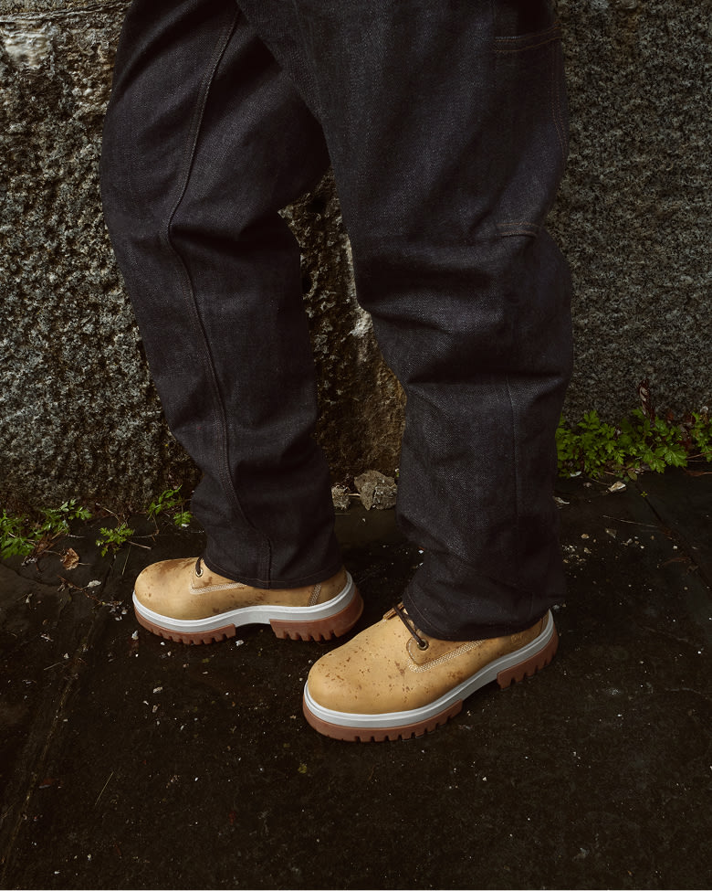 a pair of legs in dark jeans and light yellow waterproof timberland boots in a puddle