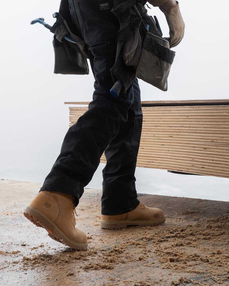 construction worker lifting wooden planks wearing steel toe boots