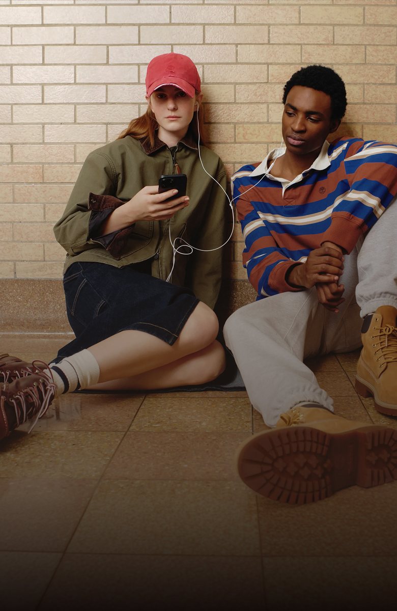 Image of two people wearing Timberland clothing sitting in a hallway listening to music.