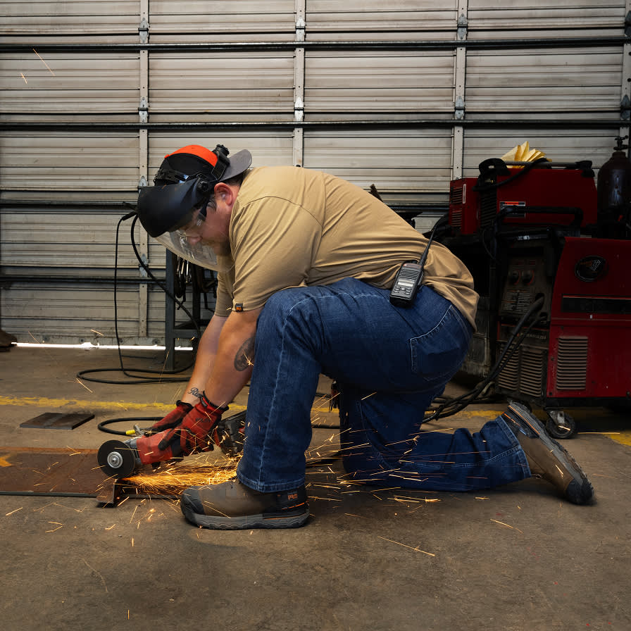 A man wearing protective gear, working on metal while kneeling.