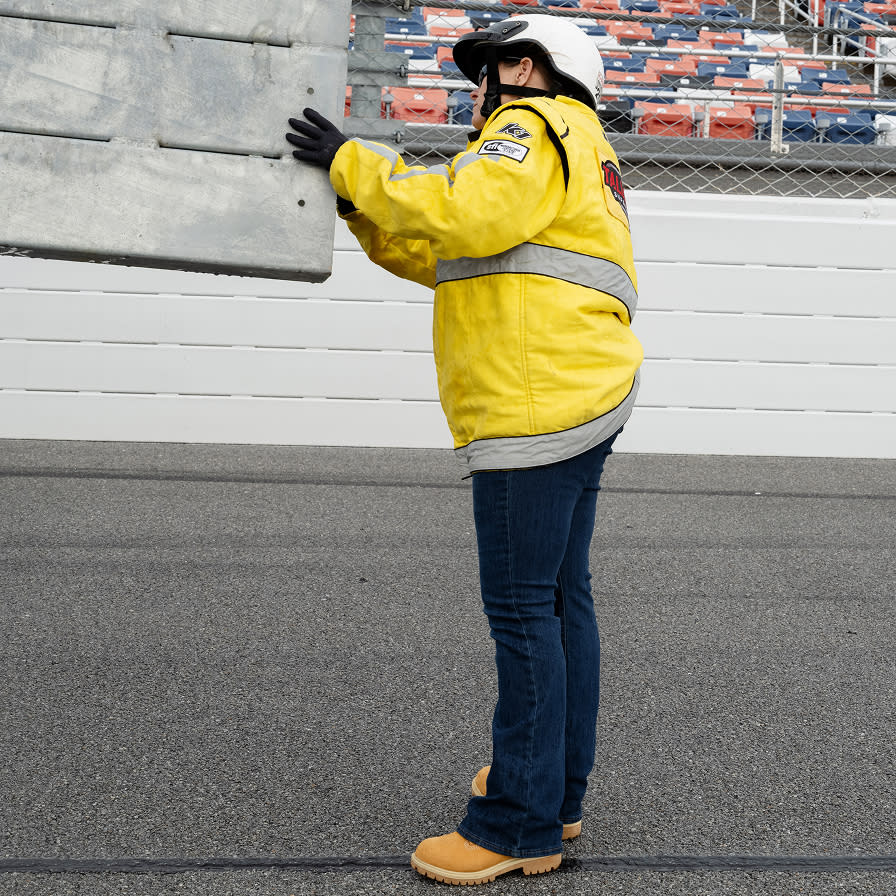A women wearing reflective work gear, guiding machinery on the race track.
