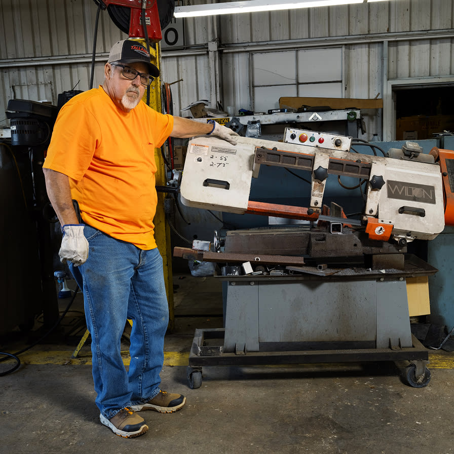 A man wearing orange, standing in a workshop with machinery.
