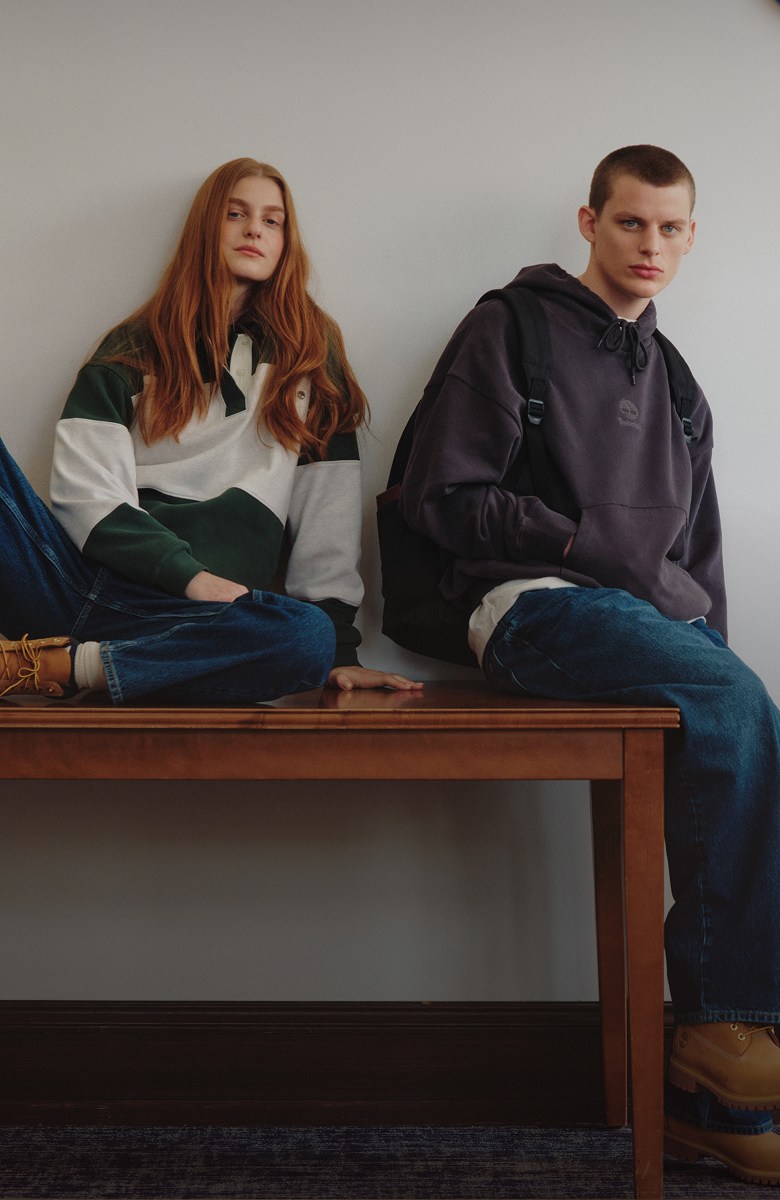 Image of two people wearing Timberland clothing sitting in a hallway listening to music.