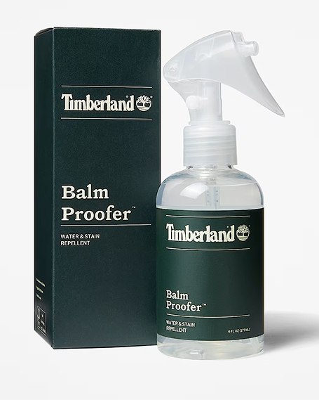A bottle of Timberland Balm Proofer Water & Stain Repellent spray with a clear plastic body and trigger nozzle, standing next to its dark green product box on a plain white background.