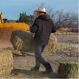 A man working on a farm raising a bale of hay.