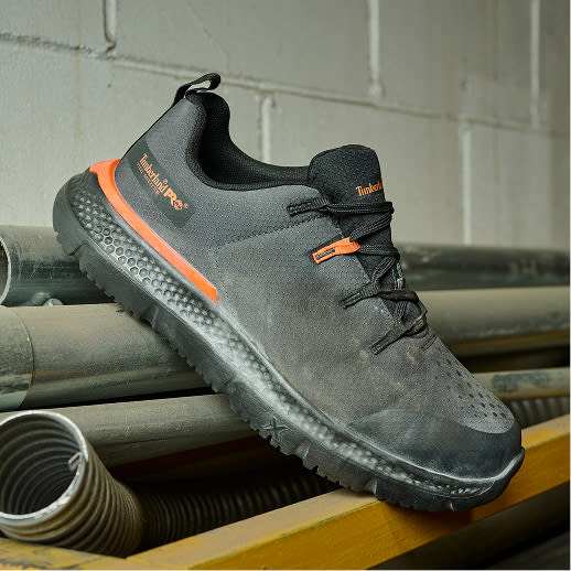 A light-weight, breathable work sneaker propped up on a pile of pipes.