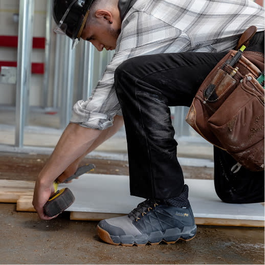 A man kneeling, taking measurements in comfortable work sneakers.