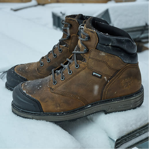 A pair of brown leather works boots resting in the snow.