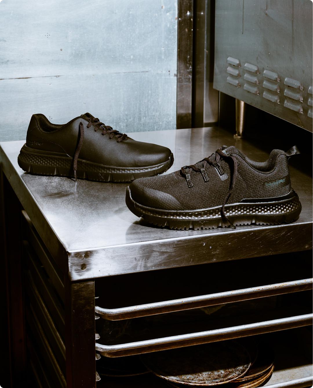 A pair of black work sneakers on a stainless steel table, in an industrial kitchen setting. 