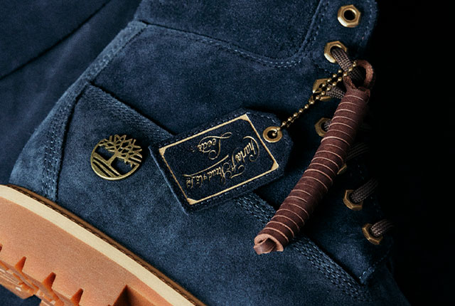 Image of the Timberland Indigo Suede 6-Inch Boot, on its side on a matching piece of dark blue suede. The boot is deep blue with golden accents and brown outsoles.