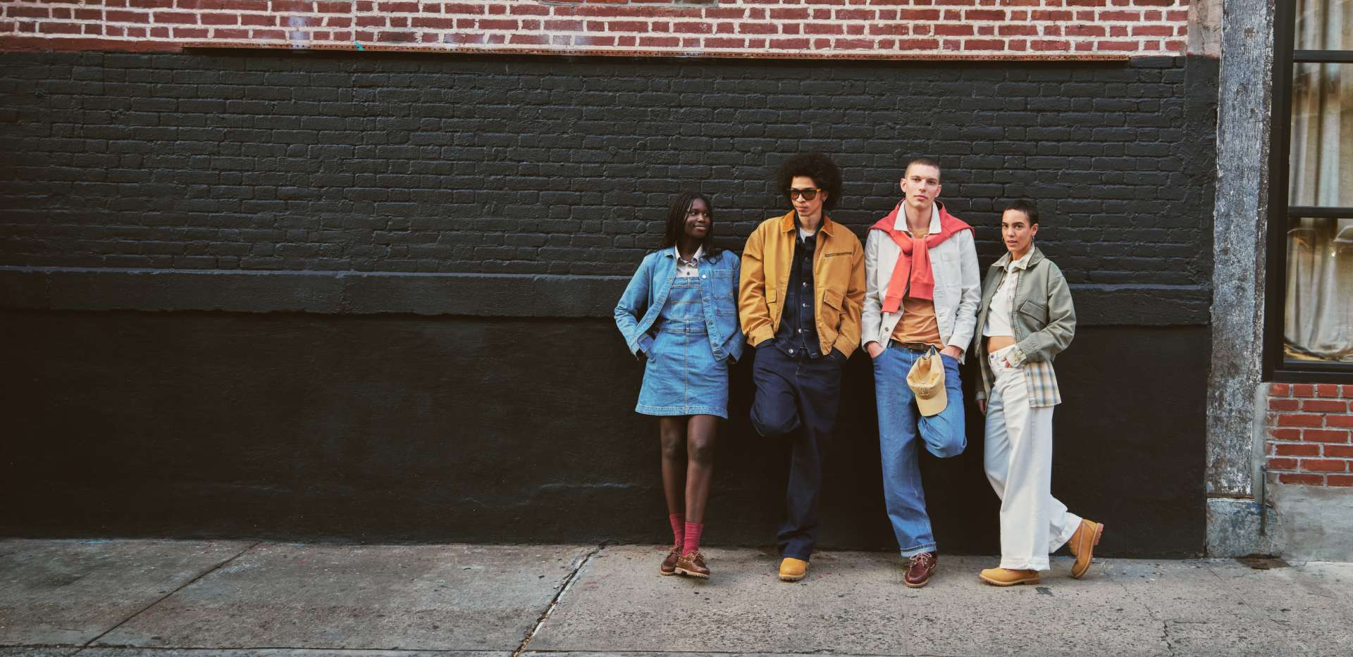Group of four friends and/or coworkers standing next to a building wearing Timberland apparel and boots.