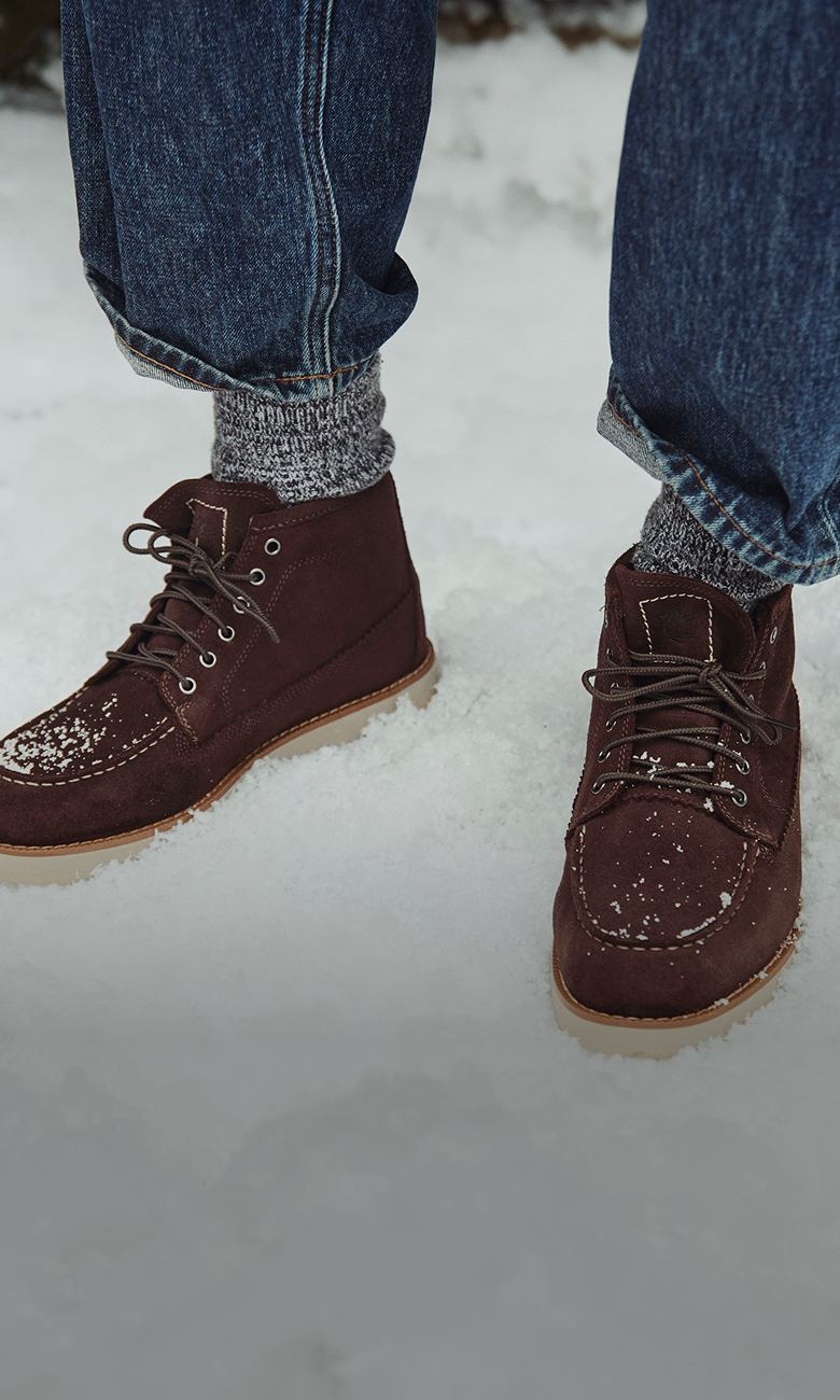 a pair of feet wearing jeans and chukka boots in the snow